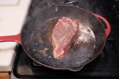 Searing meat with butter on a skillet.