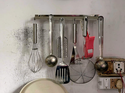 Metal spatulas and other metal utensils hanging in a kitchen rack. Photo by Ricky Singh.