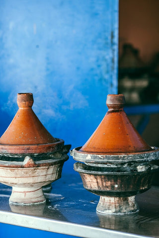 Tagines sitting on an open stove that consists of the ceramic pans the the accompanying conical ceramic lid.