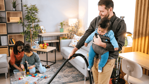 image of a father vacuuming wearing a baby in a baby cling