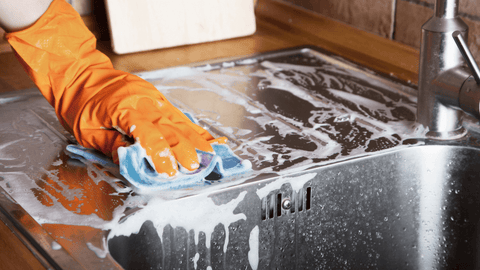 image of sink being cleaned with rubber gloves, sponge and suds