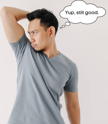 Image of a man smelling his armpit to confirm that his clothes are still clean enough to rewear