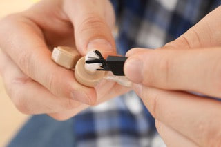Man cleaning hearing aid with brush