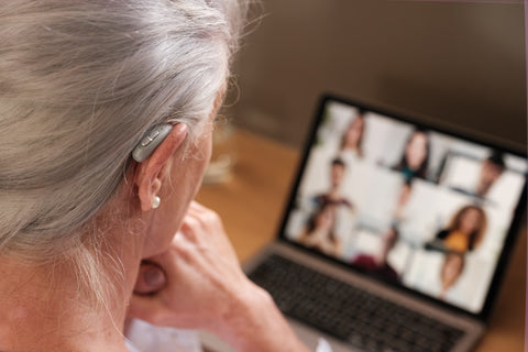 Lady on conference call with laptop screen in front of her and hearing aid in right ear