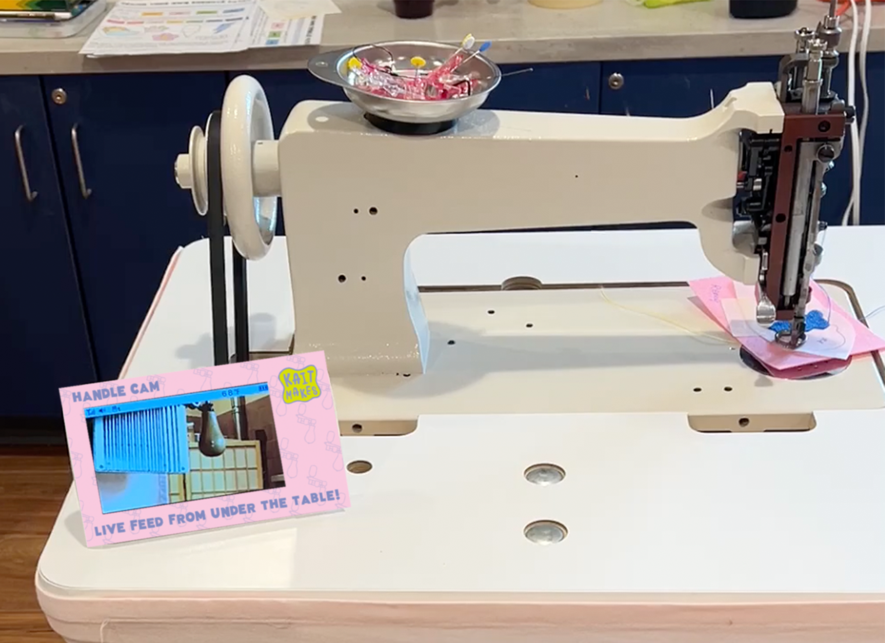 view of Kaitlyn's chainstitch embroidery machine with a small baby monitor screen next to it showing the handle under the table