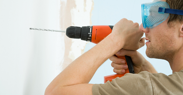 man drilling in the wall to hang metal wall decoration in his house.