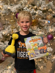 Brontie Plush Toy and Book in the hands of blond haired child with Christmas tree behind it