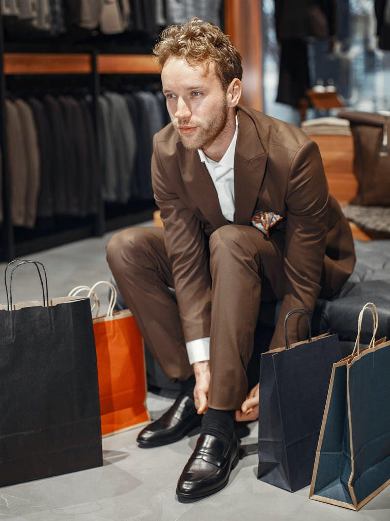 Man wearing a brown suit and trying on black shoes