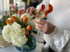 Floral arrangement with white hydrangeas, orange tulips, and calla lillies.
