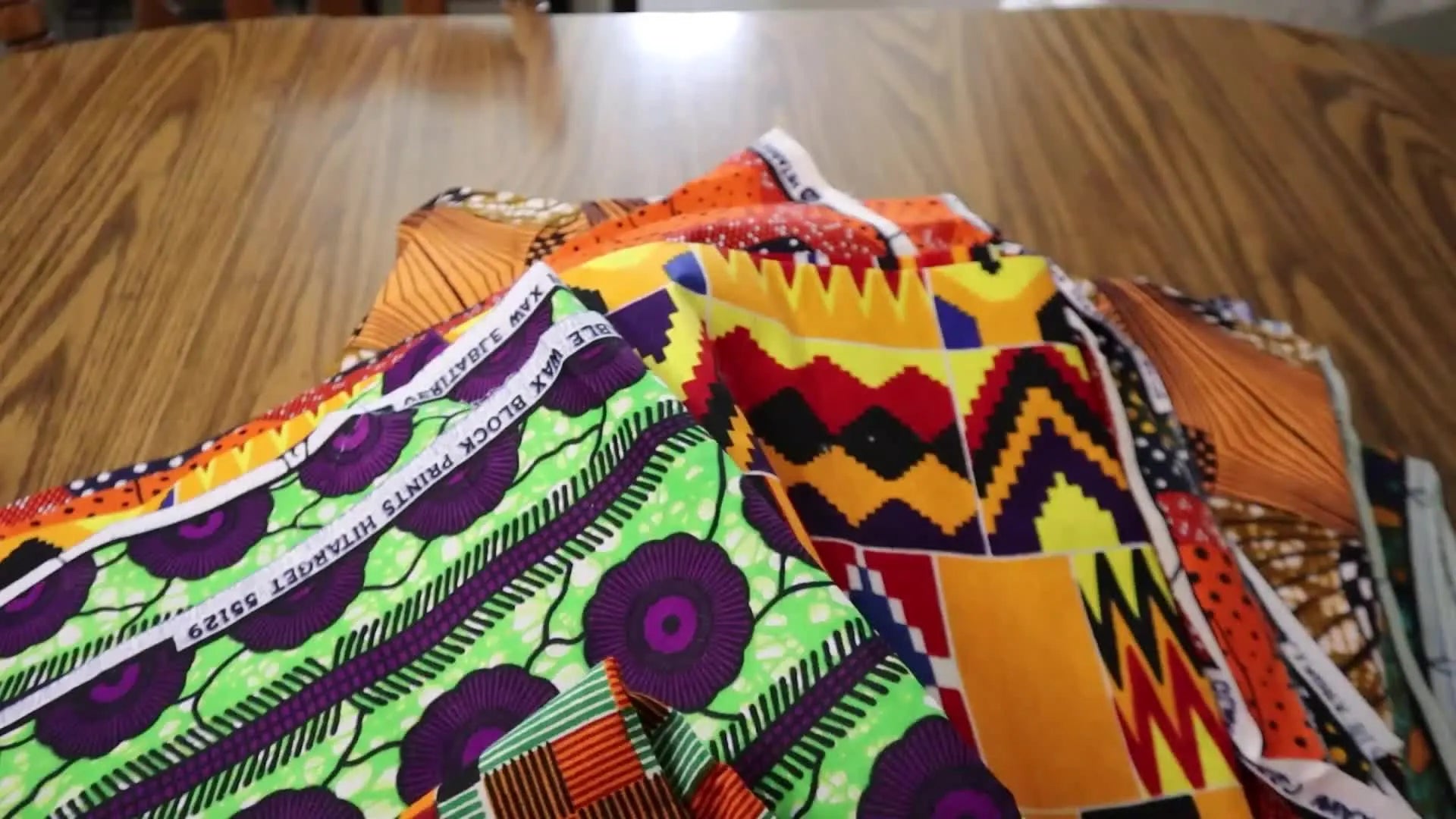 Pile of colorful African fabrics on a wooden table.