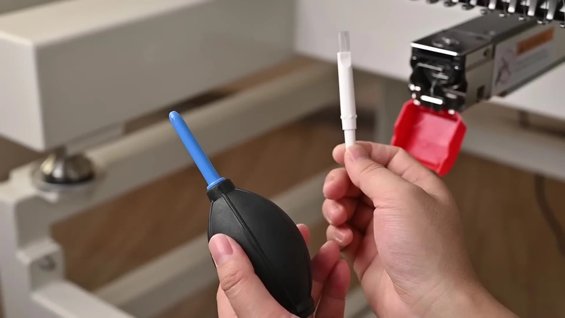 Hands holding a soft brush and compressed air duster near the machine's needle area