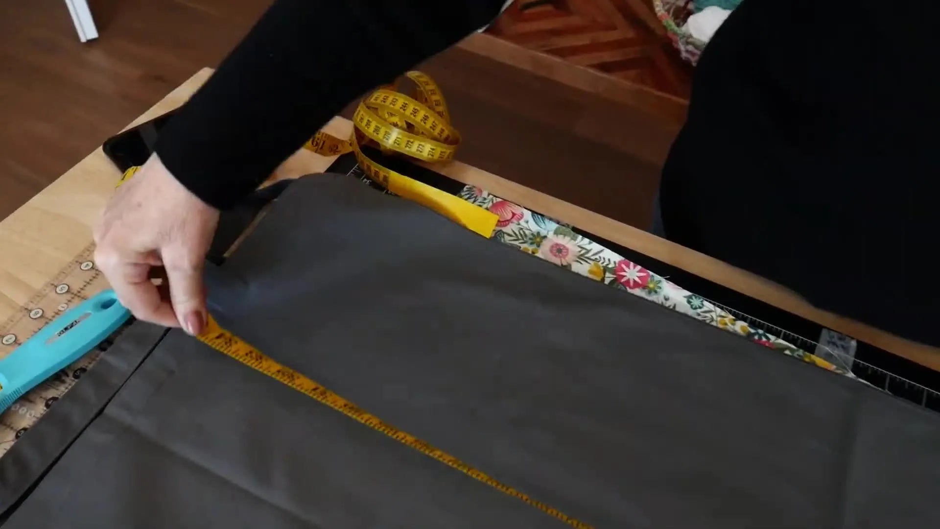 Hands using a yellow measuring tape to measure the 36-inch length of the gray tote bag blank.
