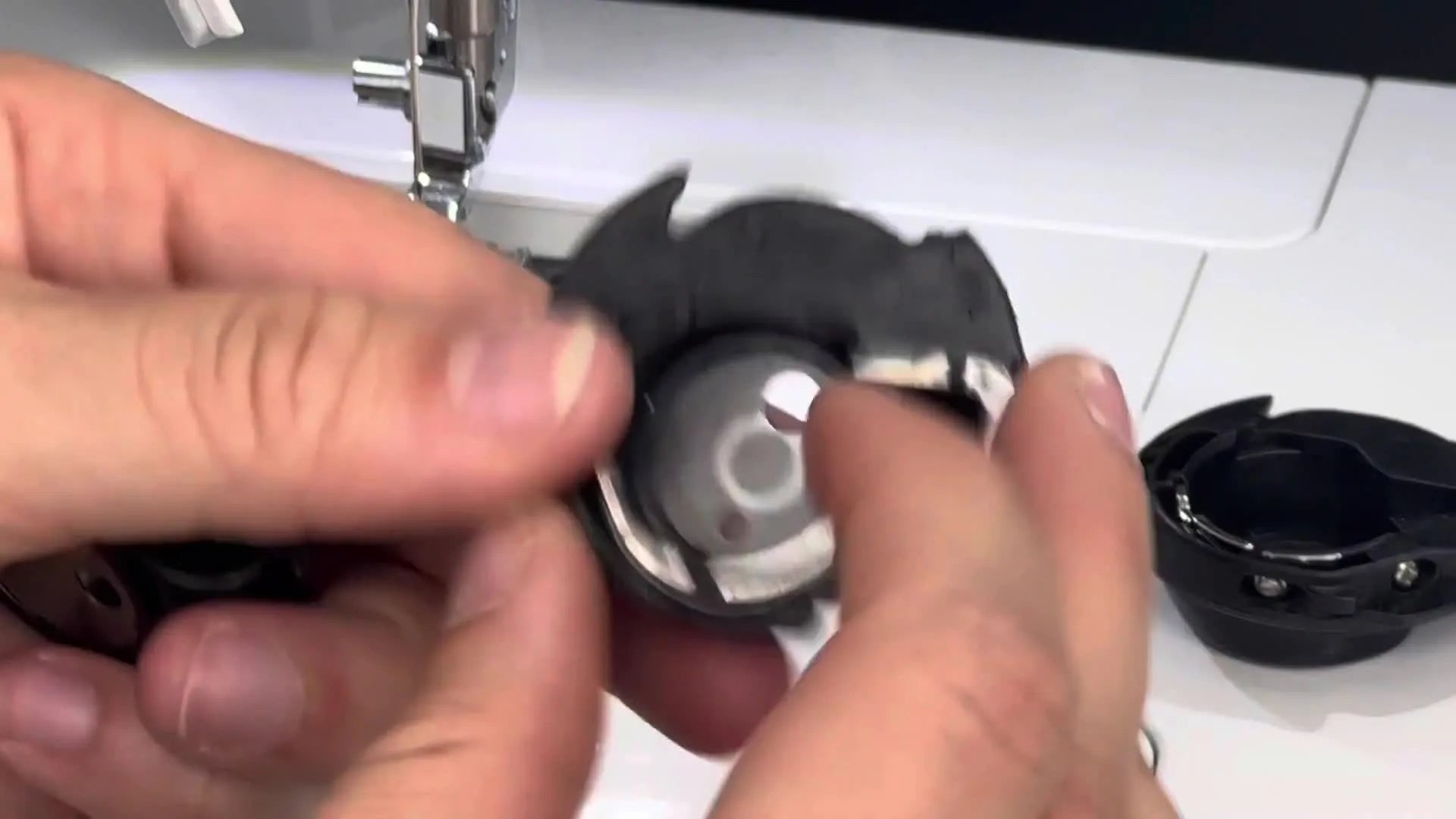 Two bobbin cases, one visibly damaged with a missing top portion and scratches.