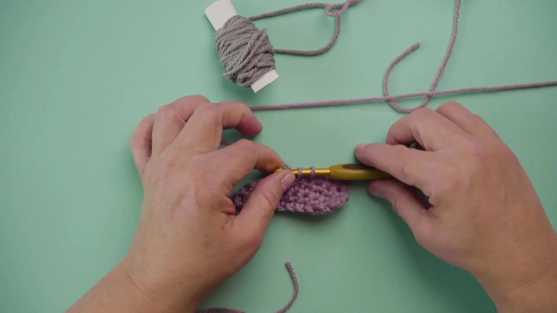 Hands reaching for the grey yarn bobbin to introduce the new color into the crochet work.