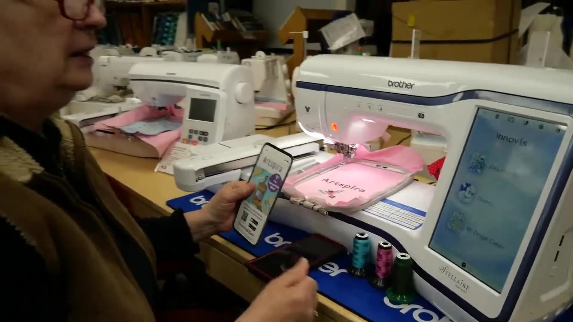 Close-up of the Brother Stellaire Innov-is XE1 embroidery machine and a smartphone displaying the Artspira app.