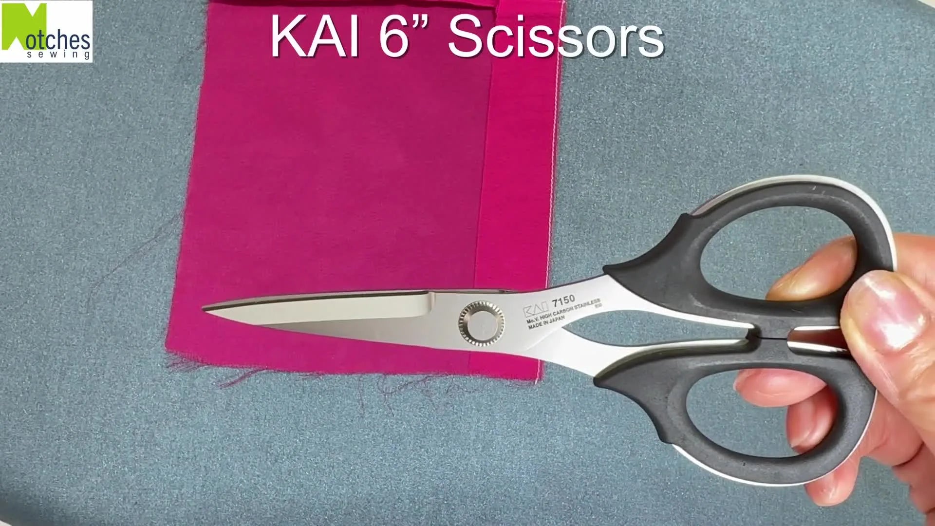 A pair of KAI 6" embroidery scissors held over pink chiffon fabric, about to trim the excess hem allowance.