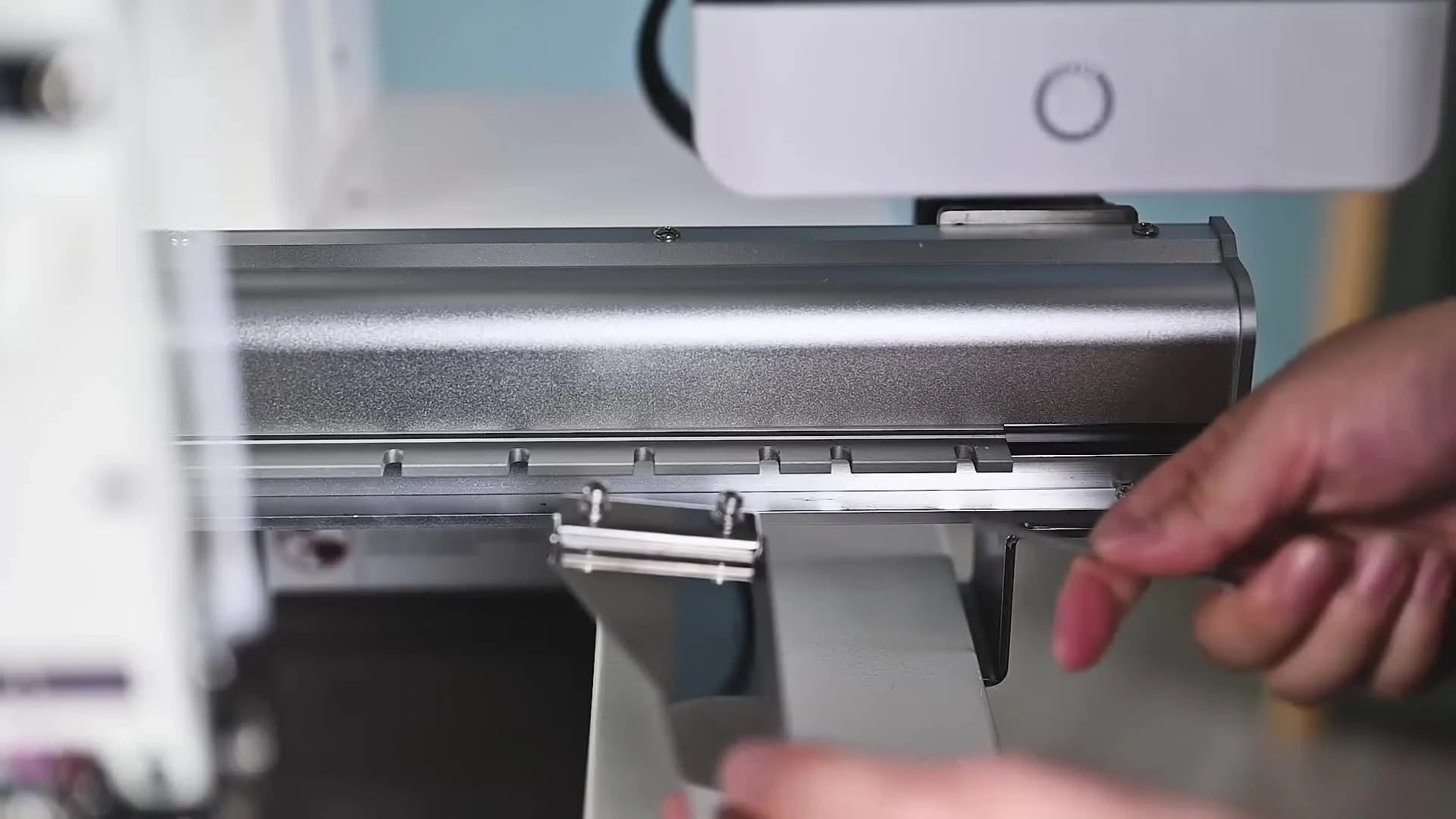 Hand using a wrench to install a handrail onto the machine's gantry rail, showing alignment with the 5th hole.