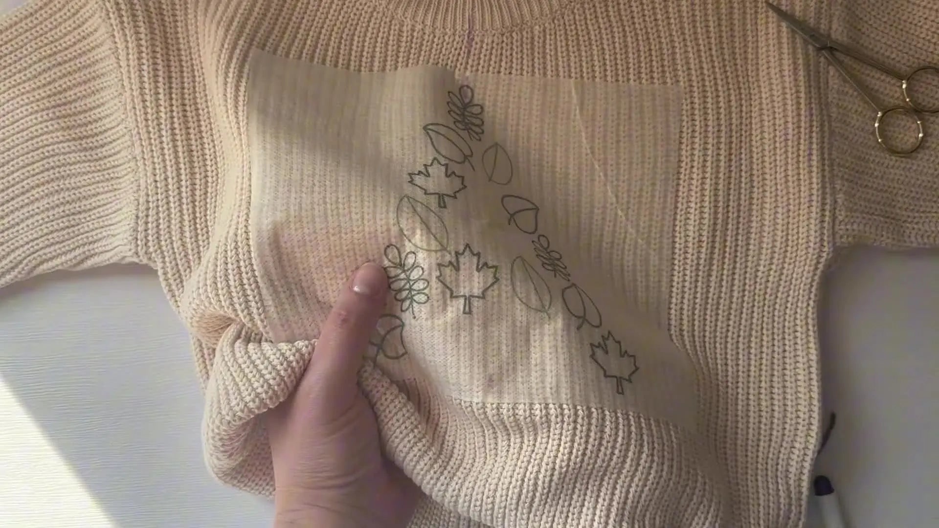 Close-up showing a needle coming up through the sweater and template to start a loop stitch on a leaf design.