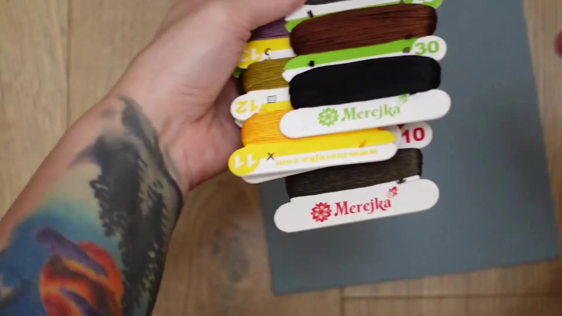 Hands fanning out multiple cardboard floss cards with various colors of thread wound around them.