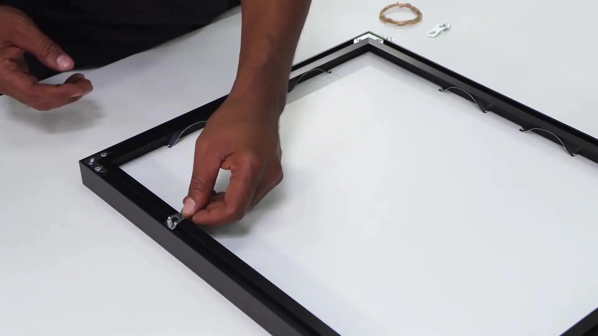 Fully assembled metal picture frame with artwork, held upright by the presenter.