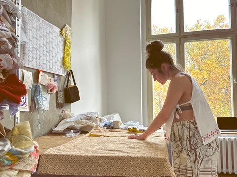 Vicki wears a childs vintage dress as a top and trousers made from bedsheets, she is working at her cutting table in her studio.