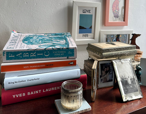 books are piled on a nightstand with a candle and photo frames.