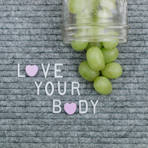 grey letter board that says love your body with a fruity mason jar pint full of green grapes