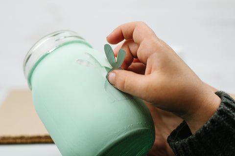 Small child's hand pulling an Easter bunny sticker off a light green painted mason jar