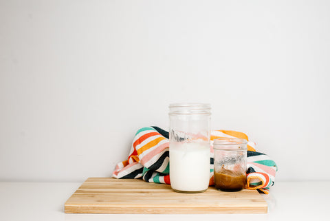 24 oz mason jar tumbler filled with ice and milk next to a smaller mason jar with freshly whipped coffee