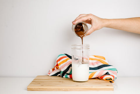 woman's hand pouring rich brown whipped coffee in to a mason jar filled with ice and cold white milk