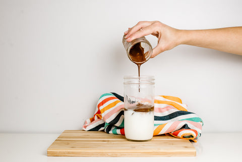 whipped coffee being poured over ice and milk in a 24 oz mason jar