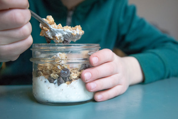 kid's hand holding a small mason jar filled with a breakfast yogurt and granola parfait