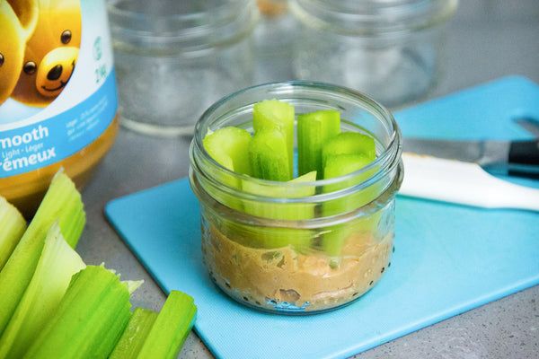a wide mouth mason jar with a layer of creamy peanut butter on the bottom and chopped celery dipped into it