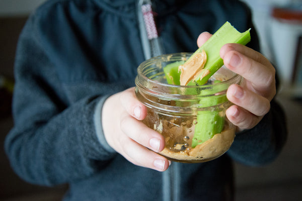 child holding a small mason jar filled with celery and peanut butter