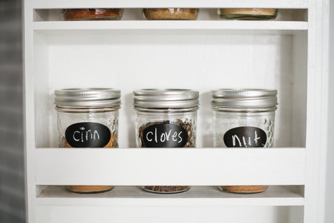 white spice rack holding three small mason jars with chalkboard labels reading cinnamon cloves and nutmeg