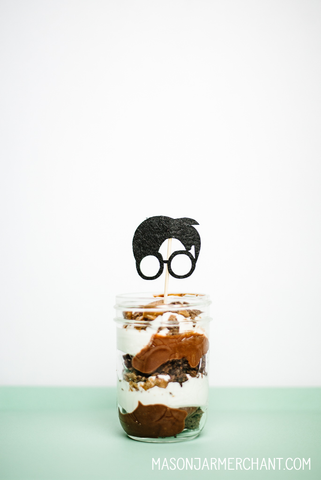 an 8-ounce regular mouth mason jar filled with layered chocolate cake, pudding and whipped cream topped with a Harry Potter silhouette cupcake topper