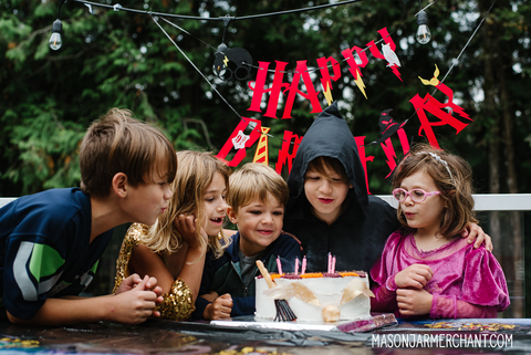 group of five kids blowing out the candles on a Harry Potter birthday cake with a red Happy Birthday banner hanging behind them