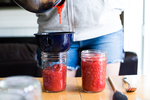 wide mouth mason jars being filled with homemade strawberry freezer jam using a metal funnel