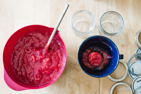 wide mouth mason jars being filled with fresh homemade strawberry jam using a metal funnel and a large spoon