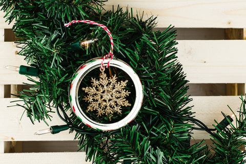 small glittery gold snowflake hanging inside a used mason jar ring with a red and white striped string