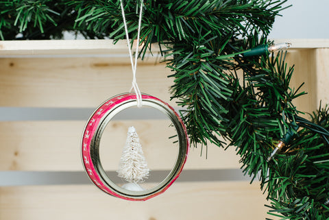 miniature white Christmas tree inside a regular mason jar ring with red and white washi tape hanging from an evergreen bough