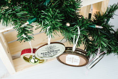 four unique handmade ornaments made from used mason jar lids and rings hanging from an evergreen bough