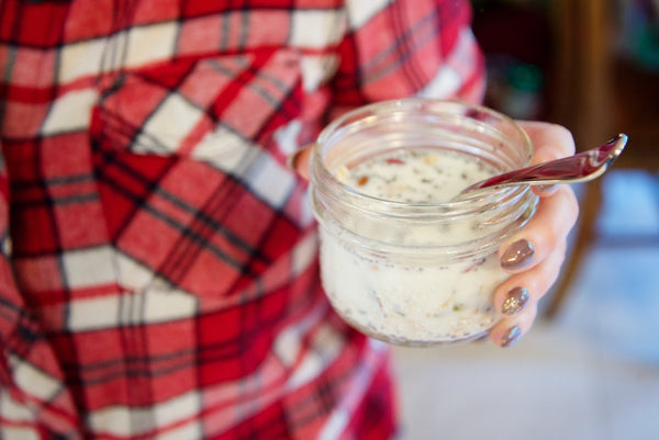 woman in a red plaid shirt holding a small mason jar full of breakfast birdseed
