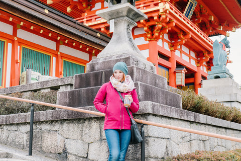 woman in pink jacket holding mason jar tumbler in front of a temple in Tokyo Japan