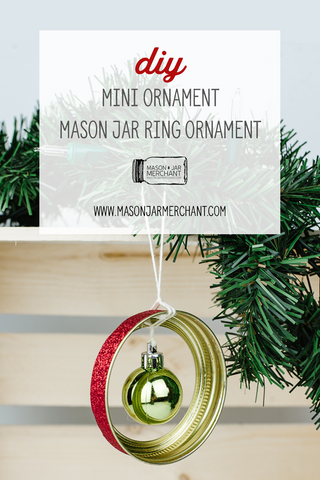 small green Christmas ornament hanging in a mason jar ring rimmed with red glitter hanging from an evergreen bow