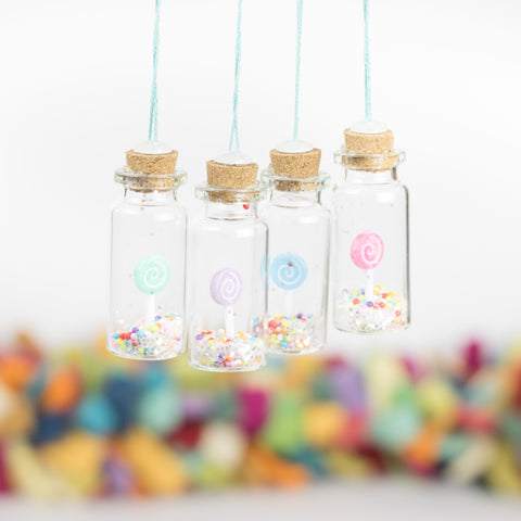 set of four handmade Christmas ornaments with tiny pastel colored lollipops and confetti tucked inside small glass bottles with cork lids