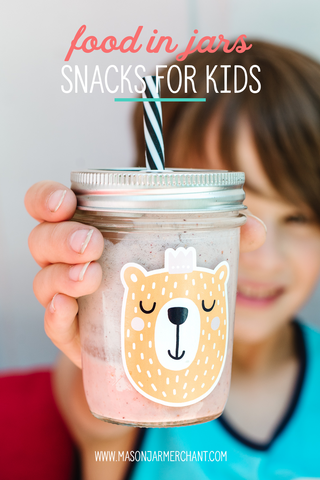 boy wearing a blue tank top and holding up a small mason jar tumbler full of a fruity pink smoothie