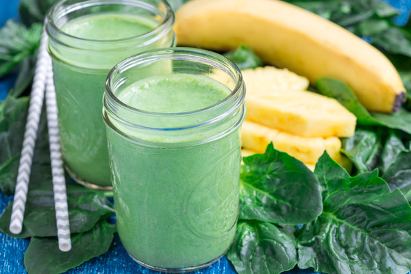 two mason jars filled with bright green smoothie next to a bunch of spinach and slices of pinapple
