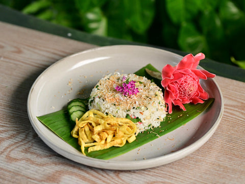 A plate of nasi ulam (mixed herb rice) plated with farm-to-table herbs and a torch ginger flower.