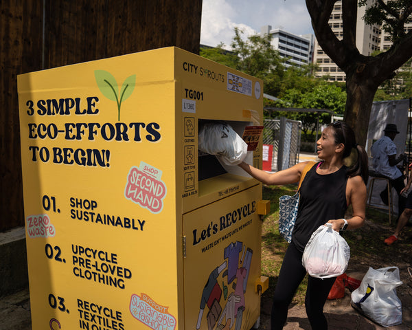 A person putting a bag of clothing into a yellow textile recycling bin set up by textile recycling company Cloop.